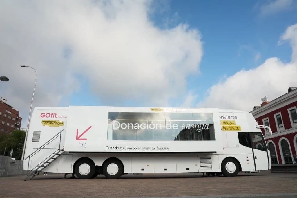 Autobús blanco de la campaña «Donación de energía», con los logos de GOfit y Technogym, aparcado en una plaza de Madrid.
