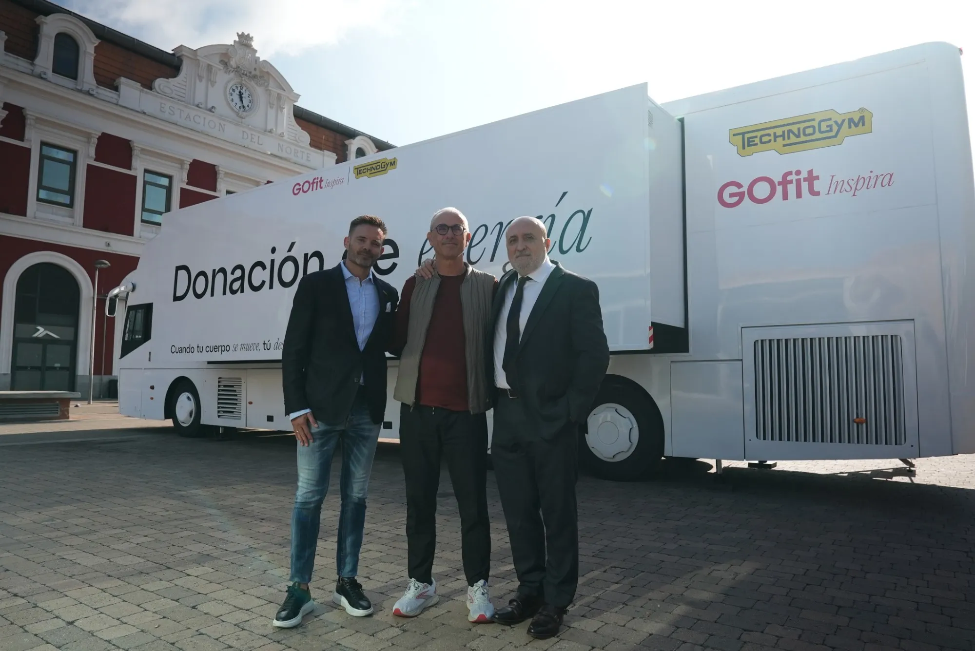 Tres hombres posan delante del autobús «Donación de energía», con el edificio de la Estación del Norte al fondo.